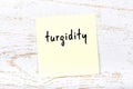 Yellow sticky note on wooden wall with handwritten word turgidity