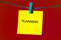 A yellow sticky note with the word Planning written in black ink is suspended from a thin blue string by a blue clothespin, set Royalty Free Stock Photo