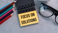 A yellow sticky note with the words Focus on Solutions written on it. A pair of glasses and a box of colored pencils are also. Royalty Free Stock Photo