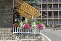 Yellow, striped retractable awning above restaurant with outdoor space for eating with flowers around the fence