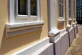 Renovated old yellow stucco house elevation closeup with new wood windows, sills and columns. Stone footing and cobble pavement