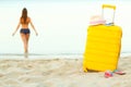 Yellow suitcase on the beach and a girl walks into the sea in th Royalty Free Stock Photo