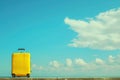 a yellow suitcase is sitting on the side of a road in front of a blue sky Royalty Free Stock Photo