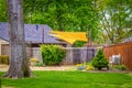 Yellow sun sails shade party area behind privacy fence of landscaped house surrounded by leafy trees