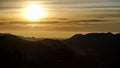 Yellow sun shining on a morning sunrise over a cloudscape on a mountain high peak silhouette