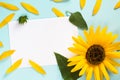 Yellow sunflower, petals and leaves on light blue background with blank white card. Floral composition, flat lay, top view,