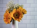 Yellow sunflowers with white babies breath floral arrangement in a ceramic white vase with a white subway tile background.