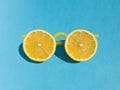 Yellow sunglasses made from fresh lemon slices and plastic lemonade straws on bright blue background. Summer minimal concept with