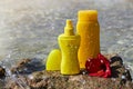 Yellow sunscreen cream bottles for skin protection with a red Hibiscus flower on a stone at the sea background. Royalty Free Stock Photo