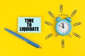 On the yellow surface there is an alarm clock, a pen and stickers with the inscription - Time to Liquidate Royalty Free Stock Photo