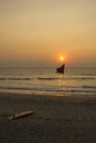 Yellow surfboard lies on the sand near the red flag against the ocean during sunset