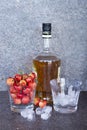 Yellow sweet cherries in a whiskey glass, ice cubes and a bottle of whiskey against a stone background. A refreshing cold cocktail Royalty Free Stock Photo