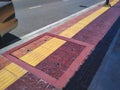 Yellow tactile paving line with brown tile floor for the blind and visually impaired on footpath in roadside area Royalty Free Stock Photo