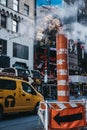 Yellow taxi drives past the steam vapour orange and white stack in New York, USA.