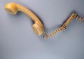 Yellow telephone receiver with twisted cord from an old antique rotary phone on blue background. Plastic removed handset