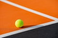 Yellow tennis ball on an orange court with white baselines and a black out-of-bound area