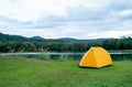 Yellow tent is set on grass field or meadow near lake with cloudy sky and it look peaceful and quiet place for people who want to Royalty Free Stock Photo