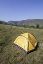 Yellow tourist tent in the grass in a meadow in the mountains
