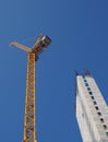 Tower crane working on a construction site with a tall concrete building against a bright blue sky Royalty Free Stock Photo