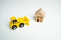 Yellow toy bulldozer and a house. Encroachment on private property. Illegal buildings and construction. Violation of building