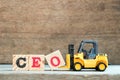 Yellow toy forklift hold block O to complete word CEO abbreviation of Chief Executive Officer on wood background