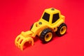 Yellow toy tractor with rake nozzle to load the forest on a red background Royalty Free Stock Photo