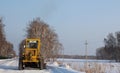 Yellow tractor grader removes snow from the road cleans travel in winter Royalty Free Stock Photo