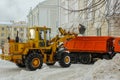 yellow tractor loads a pile of dirty snow into the truck, clearing the road, driveway after heavy snowfalls