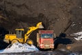 A yellow tractor loads a truck with black slag using a bucket on a black mountain background. Ecology problems