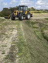 Yellow tractor mowing grass overgrowing the flood bank on the river Royalty Free Stock Photo