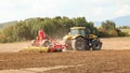 Yellow tractor pulls red sow mechanism over field, trees in background