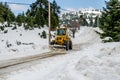 Yellow Tractor Removes Snow and Clears the Road that Passes Through the Forest in a Greek Mountain