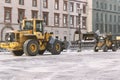 Yellow tractor Volvo and Wille clearing the snow the street in the gloomy weather