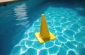 Yellow traffic cone floats in bright blue swimming pool water on sunny day. Plastic object rests on water surface creating Royalty Free Stock Photo