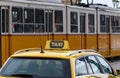 Yellow tram passing by a yellow taxi parked in street in city