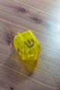 Yellow translucent plastic Hanukkah dreidel on a wood table, Hebrew letter Shin facing up