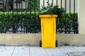 A yellow trash can with green leaves on the street beside the frence, enviroment concept