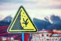 Yellow triangle outdoor warning sign on snowy mountain peaks winter background displaying man falling down a steep as safety peril