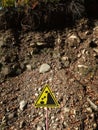 Yellow triangular warning sign stands on a hillside background