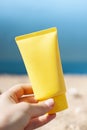 Yellow tube of sun cream in the woman`s hand on the beach close up. Royalty Free Stock Photo