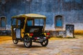 A yellow tuk tuk vehicle from the Tuk Tour company in front of an aged stone wall from a touristic church in Ouro Preto, Minas