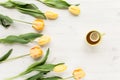 Yellow tulips, cup of tea isolated on a white, wooden background. lay flat, top view Royalty Free Stock Photo