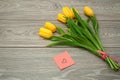 Scattered yellow tulips and colored paper sheet with a heart on a gray table. Greeting card. Royalty Free Stock Photo