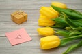 Yellow tulips lie on a gray wooden table next to a sticker on which a heart is drawn. Royalty Free Stock Photo