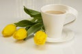 Yellow tulips lie near the cup of cappuccino