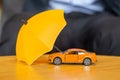 Yellow umbrella cover or protection orange car toy on table. Financial, money, refinance and Car insurance concept Royalty Free Stock Photo