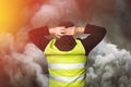 Yellow vests protests. Young man stands with his back and holds his hands on his head as a sign of obedience in tear gas