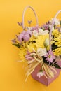 Yellow-violet flower arrangement in a box of chrysanthemums, eustomas, cotton inflorescences and dried flowers on a yellow Royalty Free Stock Photo