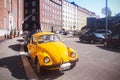 Yellow Volkswagen beetle on sunny European street against backdrop of multi-storey buildings