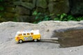 Yellow VW camper van model bus, in a nature scene, on a rock, driving out of a puddle of water.